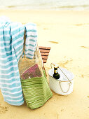 Beach bag and towel hung over chair and drink in metal bucket on sandy ground