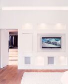 Moderner Schlafraum mit eingebautem Flachbildfernseher in Wand und offenstehende Tür zur Ankleide