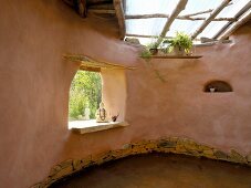 Clay house with organic lines, skylight and Buddha statue in frameless window aperture