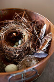 Stylised nest with feathers and various eggs in metal dish