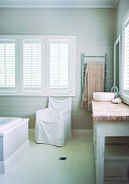 Chair with cover below window with closed shutters in rustic bathroom