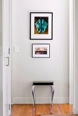 Stool below pictures on white wall of hallway