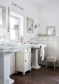 Rustic, vintage-style bathroom with twin pedestal sinks and half-height cabinet below window