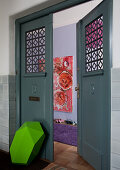 Mixture of colours and styles - grass green sculpture leaning on dove grey period door with view of pink painting and lilac rug in large, modern hallway