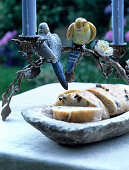 Candlestick with stylised leaf garlands and china budgerigar ornaments above stone platter of olive bread