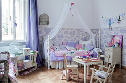 Rustic children's chairs and table in front of canopied bed in spacious child's bedroom with half-height patterned wallpaper
