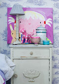 Bedside lamp and child's picture on bedside table against wallpapered wall