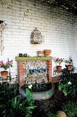 Homemade fountain in garden against whitewashed brick wall with antique decorative elements of curved wire