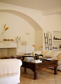Antique coffee table and white sofas in front of open fireplace in arched surround