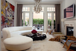 Elegantes Wohnzimmer mit überdimensionaler, weisser Couch, einem Couchtisch aus lackiertem Teakholz und weißem Flokatiboden; im Hintergrund die offene Terrassentür