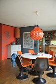 Orangerote Hängelampe über Esstisch mit Schalenstühlen aus braunem Kunststoff und orangen Polstern in offenem Wohnraum