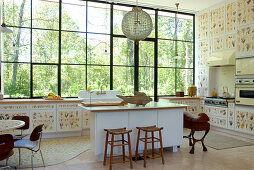 Kitchen in profusion of botanical motifs - free-standing island in front of cupboard doors covered in floral patterns and garden view through enormous windows