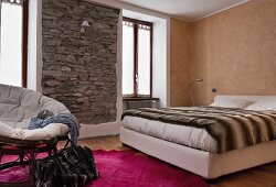 Schlafzimmer in warmen Erdtönen mit eingefasster, rustikaler Natursteinwand und einem Bettüberwurf mit Tierfellmotiv