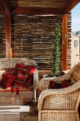 Suite of wicker furniture with red cushions below wooden pergola with bamboo screens