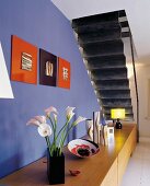 Bouquet on wooden sideboard against wall painted cobalt blue and view of black underside of folded plate staircase in modern setting