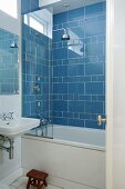 Corner of bathroom with bathtub and shower head against blue-tiled wall
