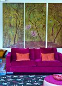 Modern couch with violet velvet cover against triptych of landscape motifs on wall