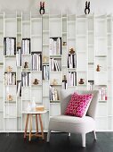 Small, upholstered armchair with cushion and side table against white, designer shelving unit