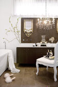 Weisser Sessel im Rokokostil und Kronleuchter mit Glasschmuck vor modernem Waschtisch mit braunem Unterschrank im Designerbad