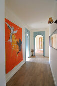 Long hallway with wooden floor, arched doorways and artworks on walls