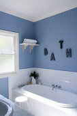 Corner of a country style bathroom with built in bath tub in front of a window and bright blue wall