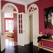 Foyer with walls painted dusky pink and view into living room through tall interior door with glass panels and arched transom window