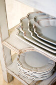 Traditional, country-house-style plates and serving platters stacked on white, vintage shelves