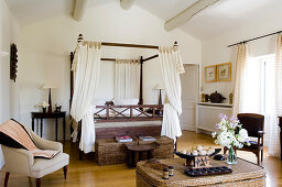 Colonial-style four-poster bed with curtains and wicker trunks in country house bedroom