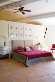 Elegant double bed with red velvet throw below collection of framed pictures on wall between bedroom and ensuite bathroom