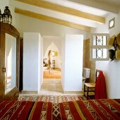 Blick über Bett mit folkloristischer Tagesdecke auf orientalischen Spitzbogen und Frau im Gang