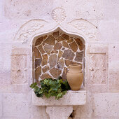 Jug and branches of leaves on masonry shelf in Oriental niche tiled with rough stone