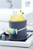 A tin can wrapped in fabric being used as a pin cushion