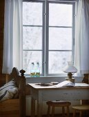 Tisch vor Fenster mit weißem Vorhang in schlichtem Schlafraum