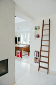 Old wooden ladder leaning on wall next to wide doorway showing view of modern kitchen beyond