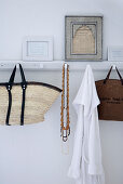Wicker shopping bag and necklaces hung from vintage-style, white-painted hook rack with framed, written pages on top