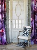Upholstered chair with cushion in front of curtained window