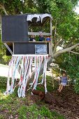 Children in modern, black tree house with ribbon curtain and boy on swing