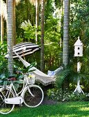 Bicycle, hammock strung between tropical trees, parasol and bird house