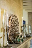 Lit candles in silver candlesticks and basketwork platter on wooden shelf