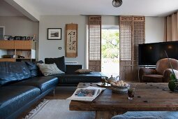Black leather sofa combination next to rustic coffee table and quaint wooden sliding elements in front of terrace door in open-plan interior
