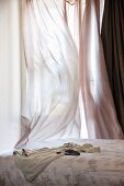 Bed in front of window veiled in fluttering, airy curtains