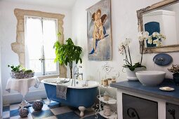 Badezimmer mit Waschtisch aus Holz, frei stehender Badewanne und blau-weissen Bodenfliesen