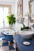 Badezimmer mit Waschtisch aus Holz, frei stehender Badewanne und blau-weissen Bodenfliesen