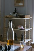 Collection of stone ornaments and books on delicate shelves; bottle and liqueur glass in foreground