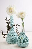 Two vases with crocheted covers holding one white carnation each