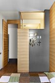 Modernes Schlafzimmer mit beleuchtetem Badeinbau und teilweise mit Holz verkleidet - Devotionalien an grau getönter Wand aufgehängt