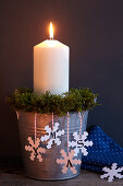 Lit candle in metal bucket with Christmas decorations