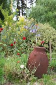 Clay amphora in front of flower bed with a riot of growth and trees in the background