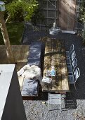 View down onto table made of rustic wooden timbers and metal terrace chairs on gravel floor in sunny urban garden