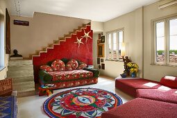 Comfortable, red sofa combination and colourful, ethnic-style rug in simple interior with staircase